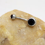 Hypoallergenic titanium steel belly ring with two black gemstone beads resting on a textured, light-colored stone.