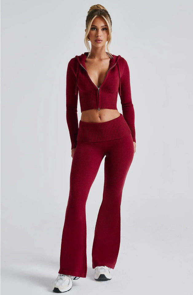 Model in a burgundy ribbed knit set: zip-up cropped hoodie and matching high-waisted flared pants against gray.