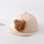 Beige ribbed corduroy baby baseball cap featuring a cute, fuzzy brown teddy bear patch on the front.