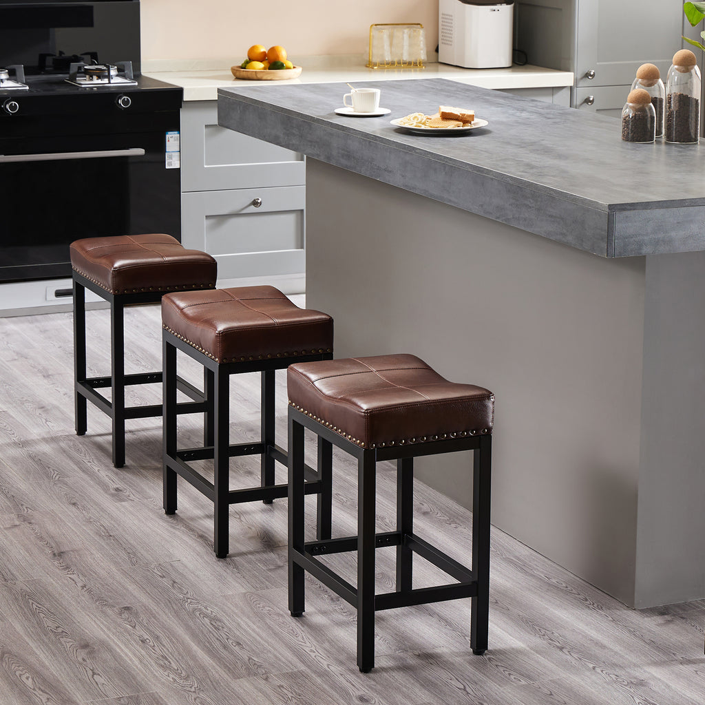 Three brown faux leather saddle bar stools with black steel frames and nailhead trim in a modern kitchen.