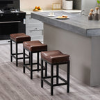 Three brown faux leather saddle bar stools with black steel frames and nailhead trim in a modern kitchen.