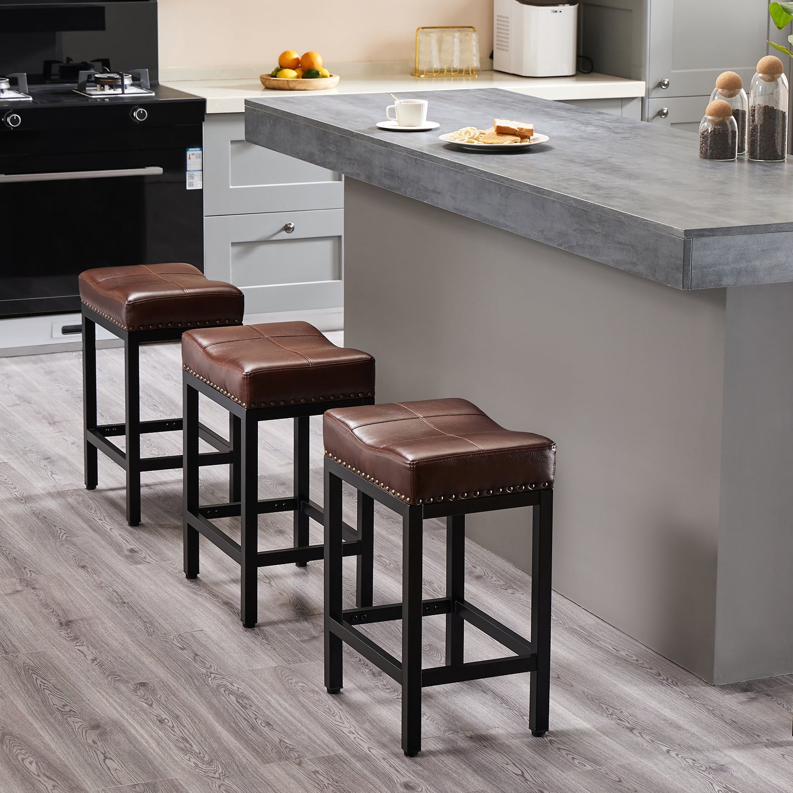 Three brown faux leather saddle bar stools with black steel frames and nailhead trim in a modern kitchen.