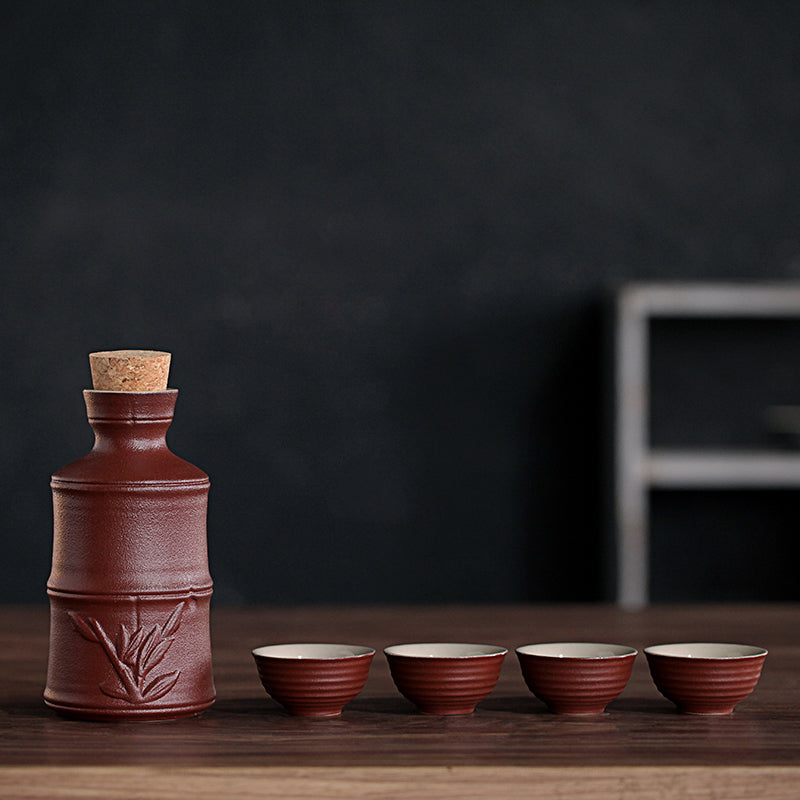 Dark brown ceramic sake set with bamboo detail, cork stopper, and four matching ribbed cups on a wooden table.