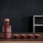 Dark brown ceramic sake set with bamboo detail, cork stopper, and four matching ribbed cups on a wooden table.