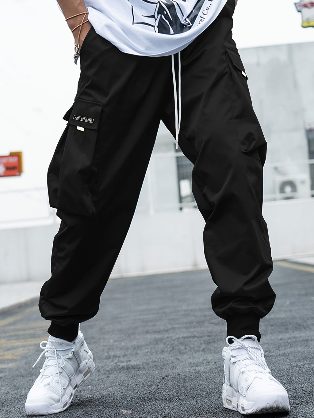 Black, loose-fit cargo pants with drawstring waist, large side flap pockets, and cuffed ankles for a streetwear look.