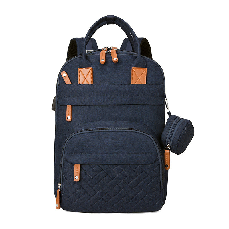 Navy blue fabric diaper backpack with tan leather accents, quilted front pocket, and an attached small pouch.