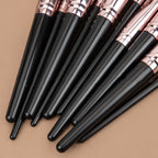 Set of makeup brushes with glossy black handles and metallic rose-gold ferrules on a tan background.