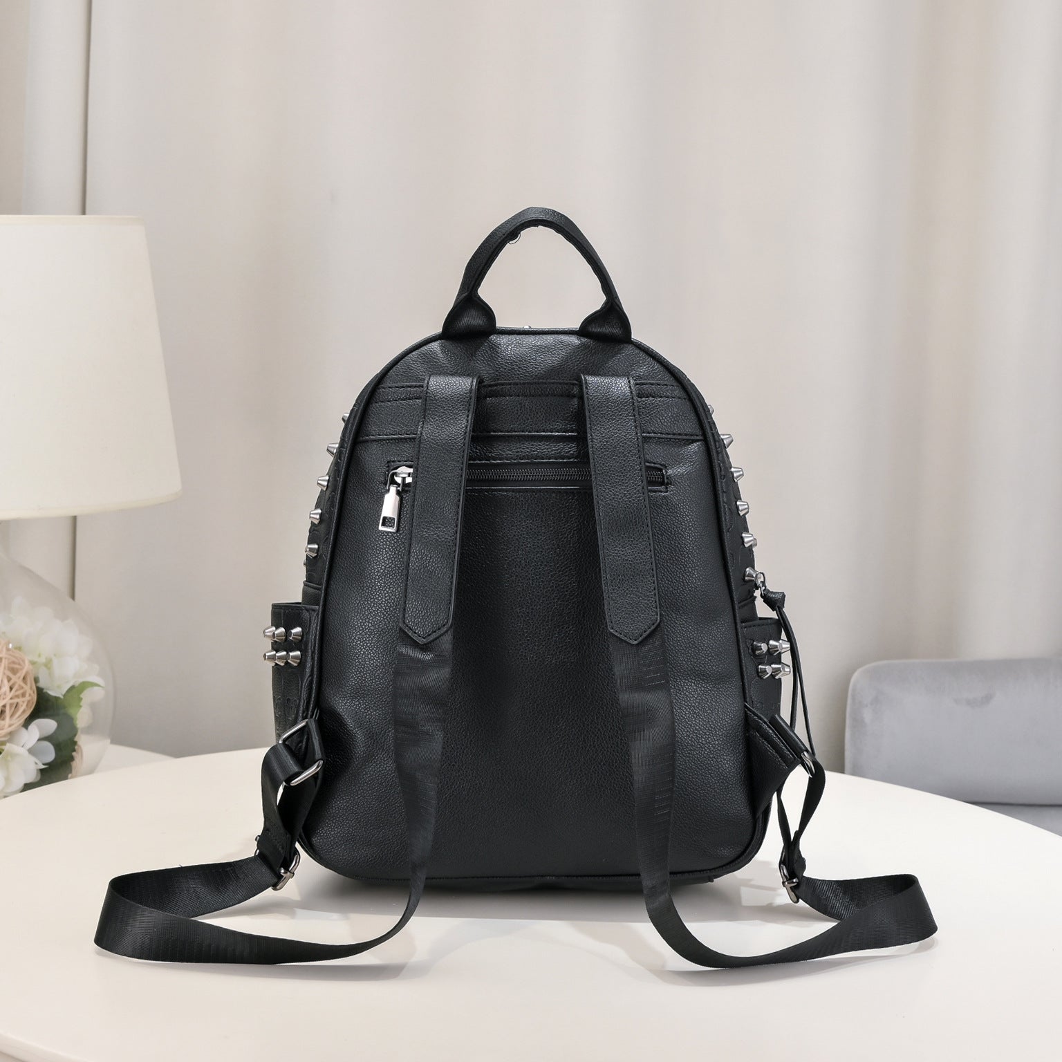 Black soft leather leisure backpack with silver rivets, adjustable straps, and a zippered back pocket.