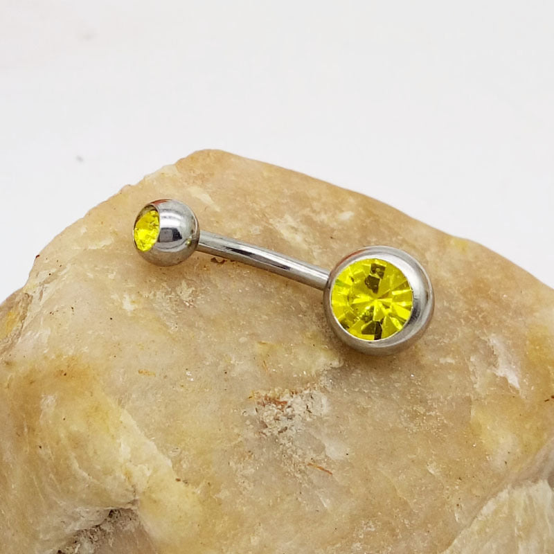 Hypoallergenic titanium steel navel barbell with two vibrant, faceted yellow crystal gems on a rough beige stone.