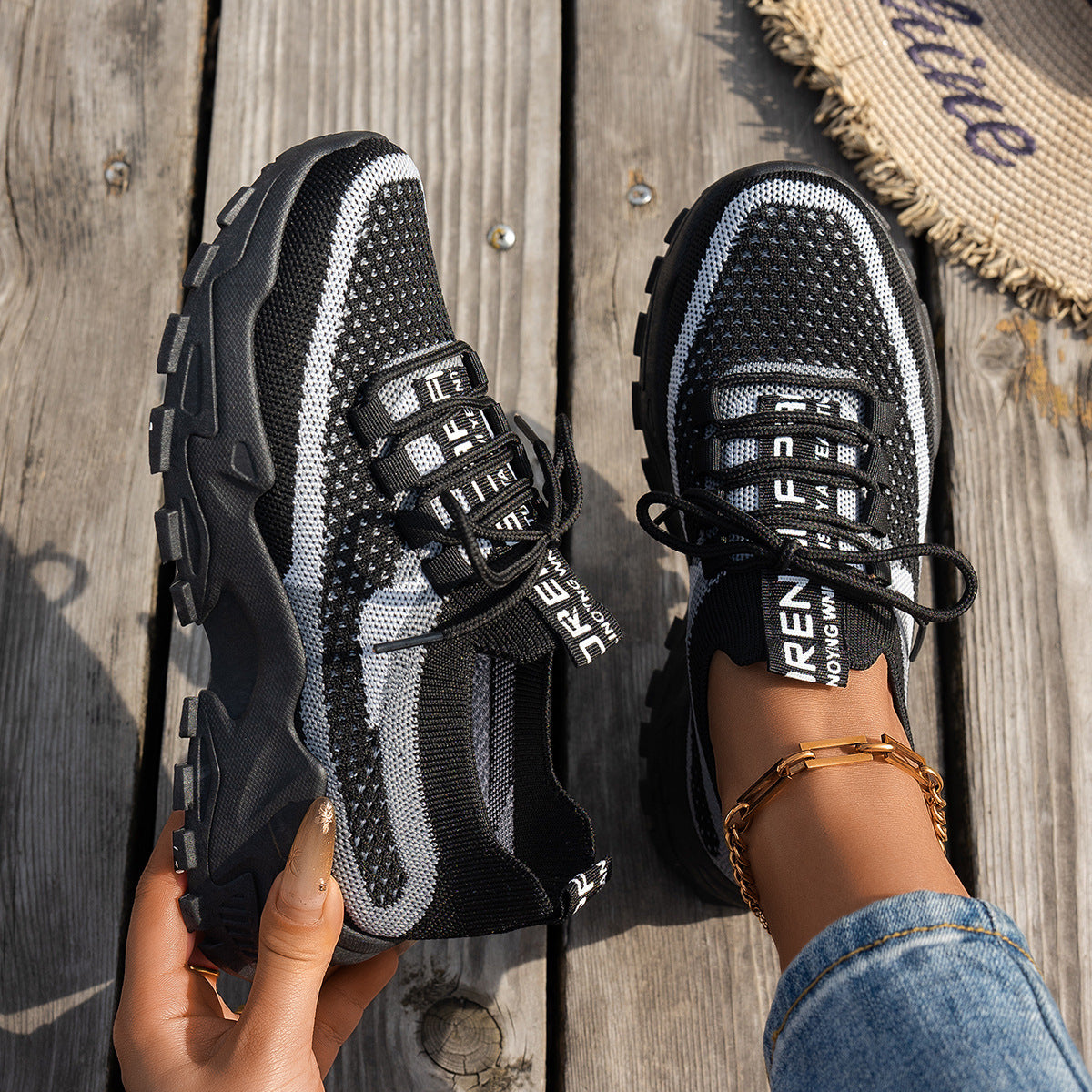Black and white knit sneakers with chunky black soles, lace-up fronts, and branded straps on a wooden surface.