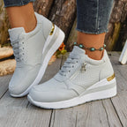 Light gray perforated athletic sneakers with side zips, thick white platform soles, and gold heel accents.