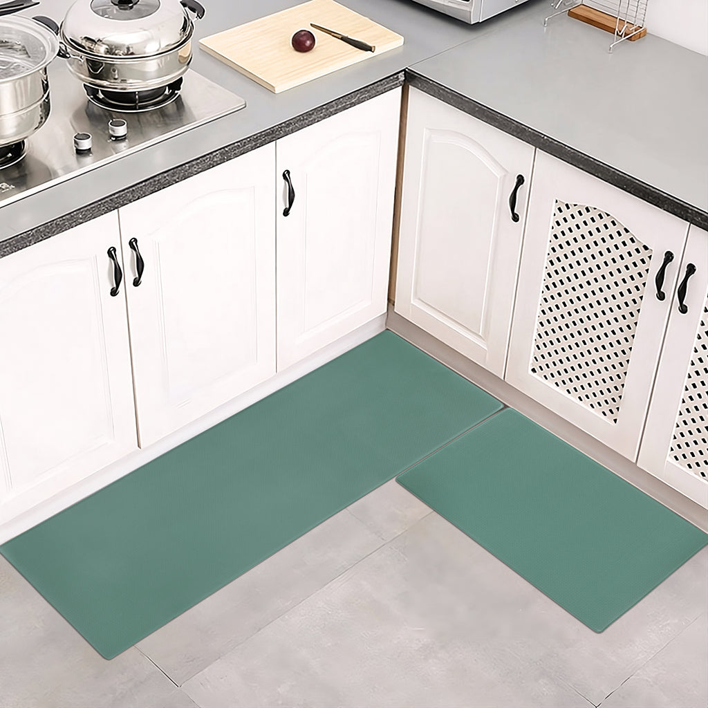 A two-piece set of solid sage green, waterproof, non-slip kitchen floor mats in front of white kitchen cabinets.