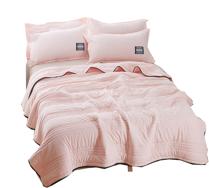 Soft pink, quilted summer bedding set with matching pillows on a bed, featuring a lightweight, cooling fabric design.