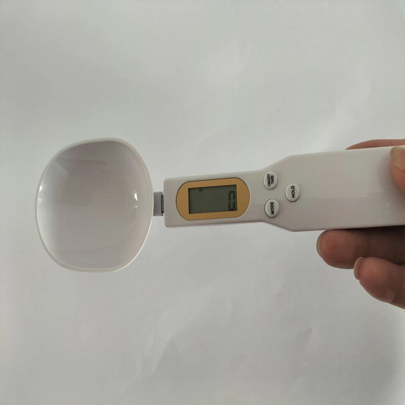 White digital spoon scale held in hand, featuring an LCD display screen and three control buttons on the handle.