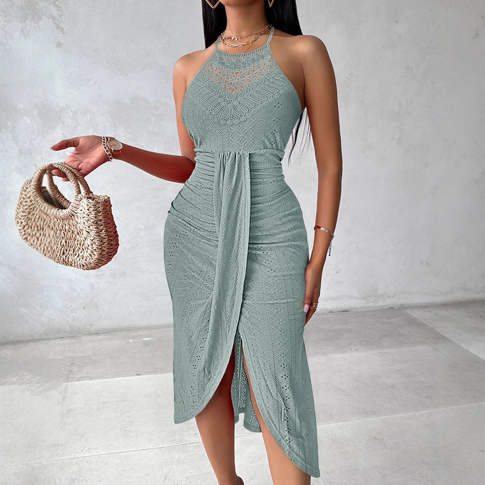 Sage green halter sleeveless midi dress in lace with an asymmetric draped front, holding a woven straw handbag.