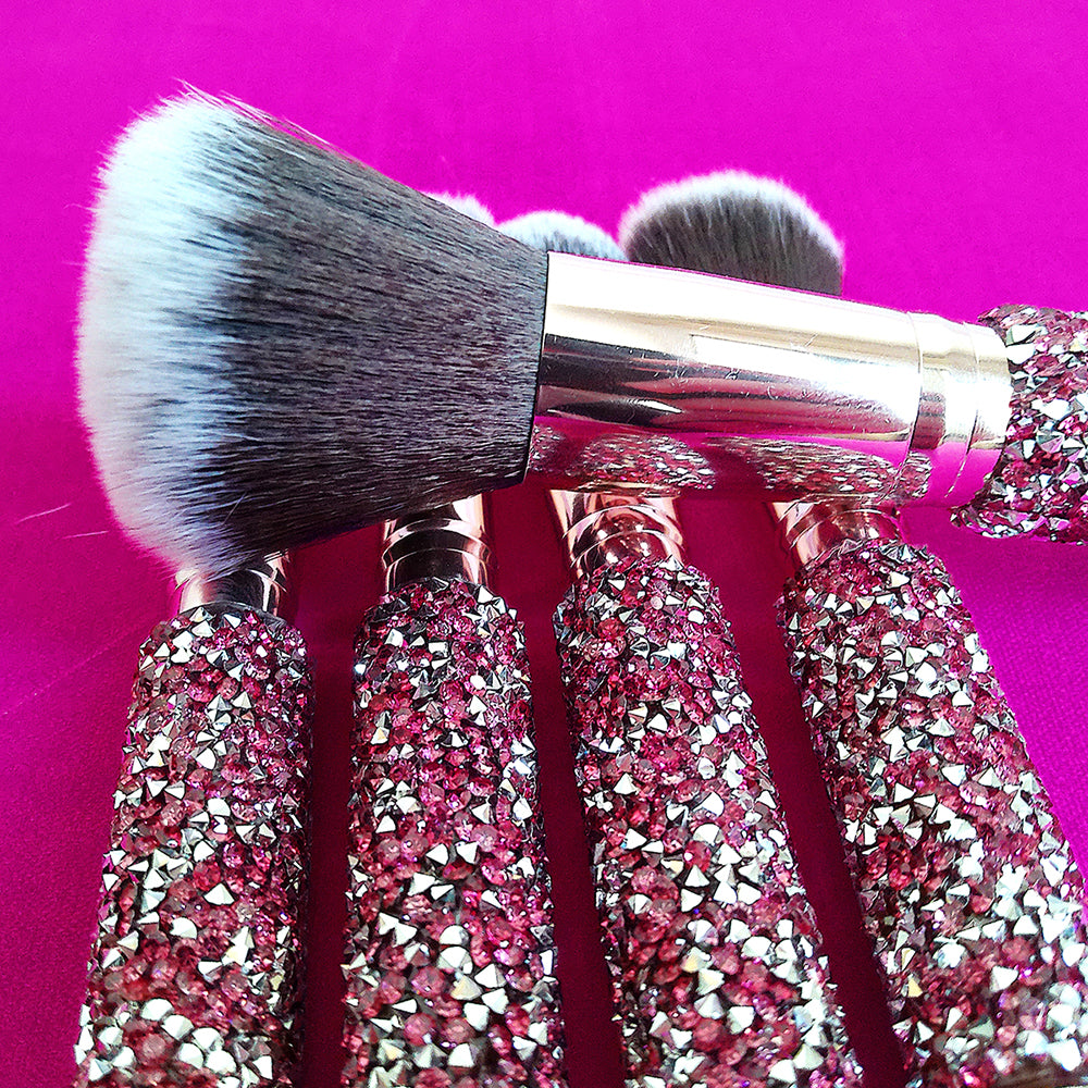Makeup brushes with pink rhinestone-inlaid handles, gold ferrules, and soft, two-tone black and white synthetic bristles.