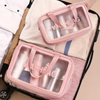 Two pink, clear-windowed "WASHBAG" travel organizers packed inside a suitcase with clothing.
