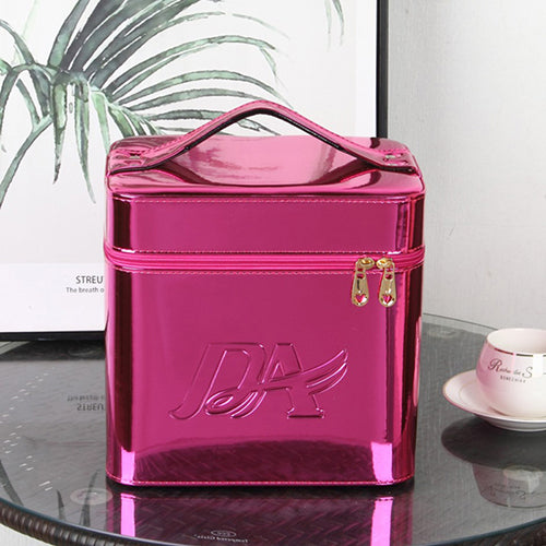 Metallic pink square makeup bag with a top handle, zippered closure, and embossed logo on a glass table.