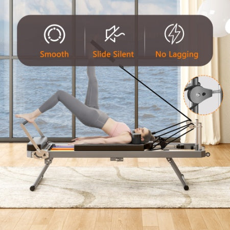 Black foldable Pilates reformer machine with a padded sliding bed, metal frame, and pulley system on a rug.