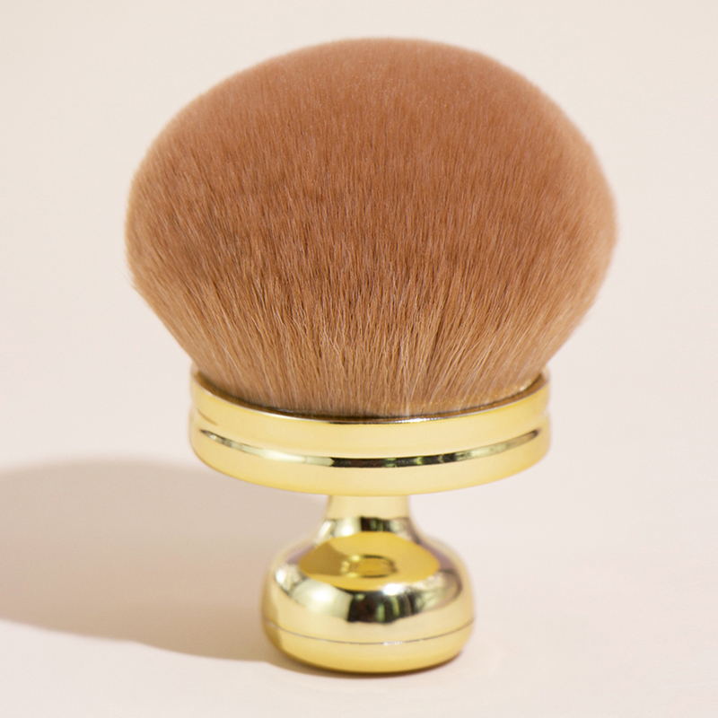 Oversized makeup brush with a large, soft, tan-colored powder head and a shiny, metallic gold handle.